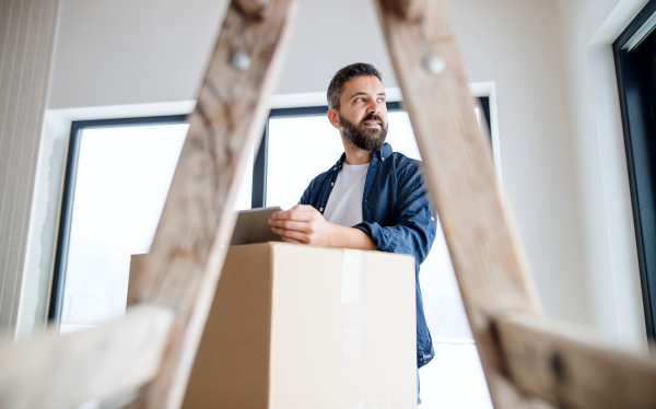 A mature man with tablet and cardboard boxes furnishing new house. A new home concept.