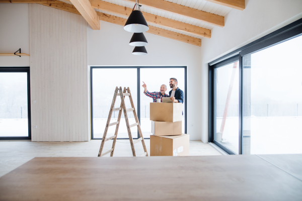 A cheerful senior man with tablet helping his mature son with furnishing new house, a new home concept.