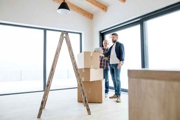 A cheerful senior man with tablet helping his mature son with furnishing new house, a new home concept.