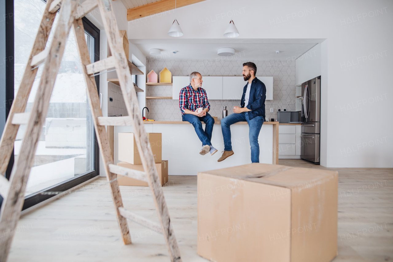 A portrait of mature man with his senior father drinking coffee when furnishing new house, a new home concept. Copy space.