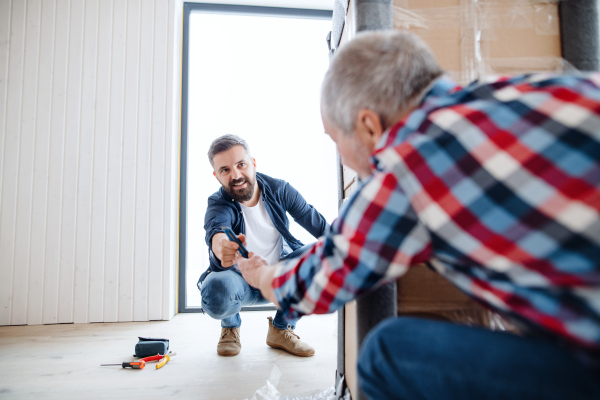 A cheerful senior man helping his mature son with furnishing new house, a new home concept.