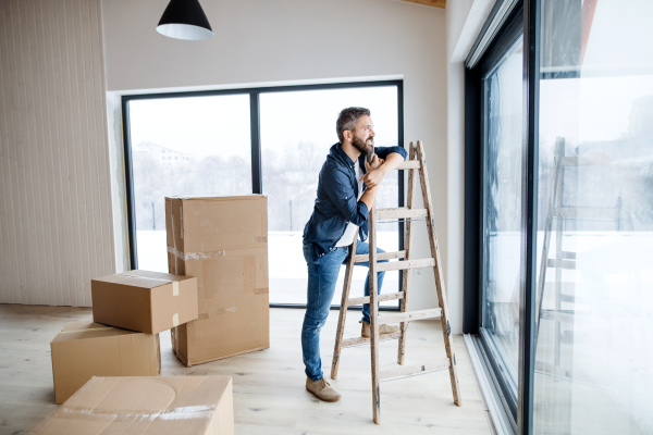 A mature man with cardboard boxes standing by a window, furnishing new house. A new home concept. Copy space.