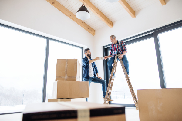 A cheerful senior man helping his mature son with furnishing new house, a new home concept.