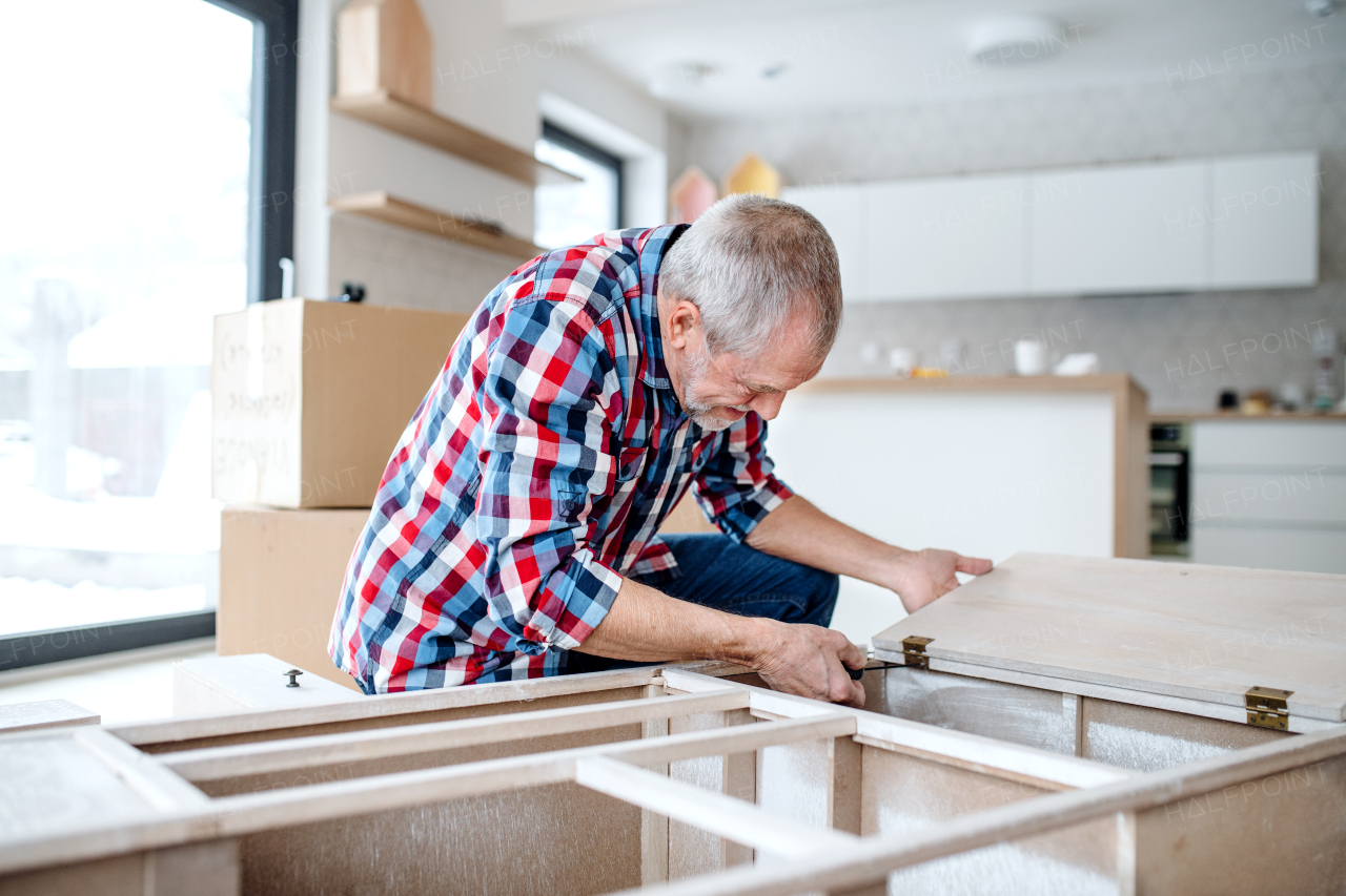 A senior man assembling furniture at home, a new home concept.