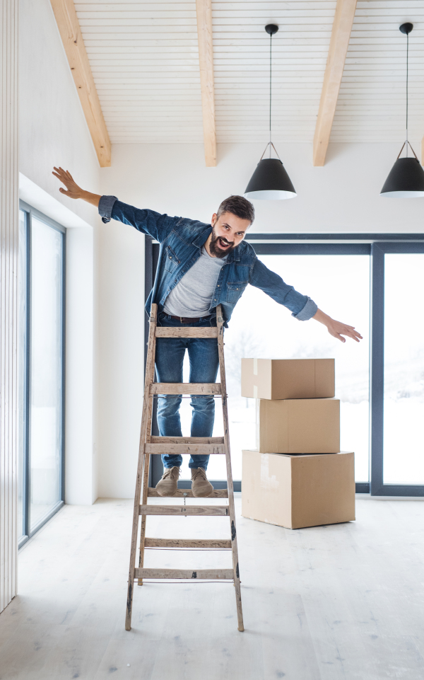 A mature man with cardboard boxes standing on a ladder, furnishing new house. A new home concept. Copy space.