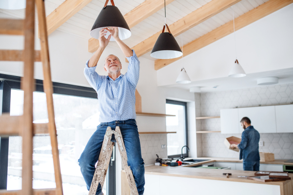 A cheerful senior man helping his mature son with furnishing new house, a new home concept.