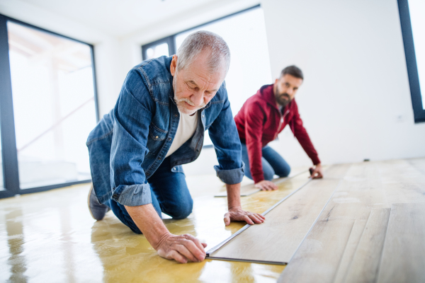 A rear and top view of mature man with his senior father laying vinyl flooring, a new home concept.