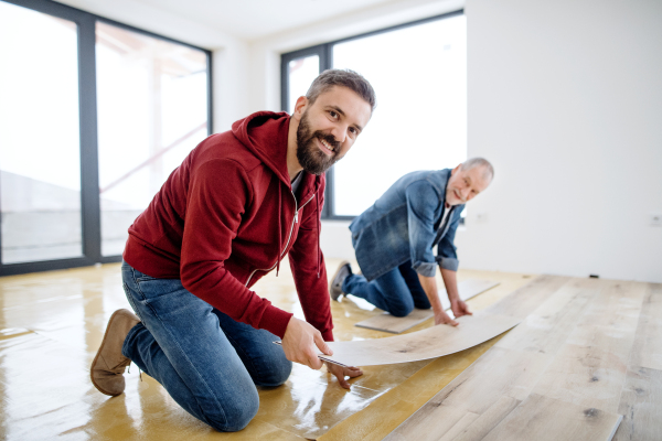 A rear and top view of mature man with his senior father laying vinyl flooring, a new home concept.