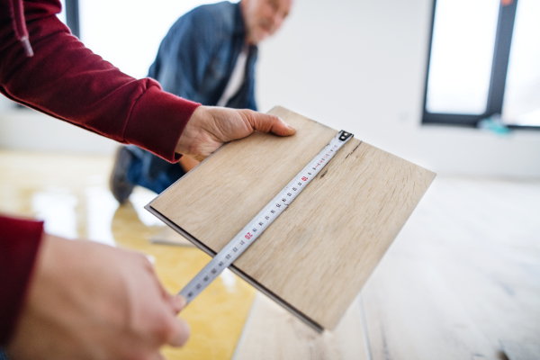 A midsection of view of unrecognizable mature man with his senior father laying vinyl flooring, a new home concept.