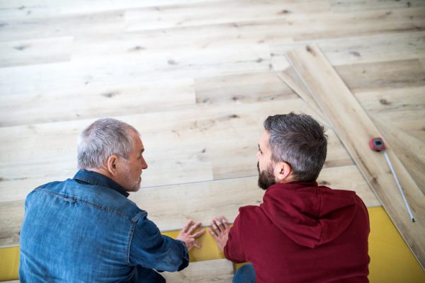 A rear and top view of mature man with his senior father laying wood flooring, a new home concept.