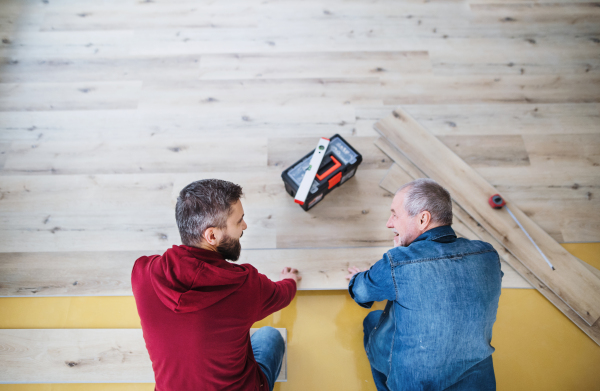 A rear and top view of mature man with his senior father laying wood flooring, a new home concept.