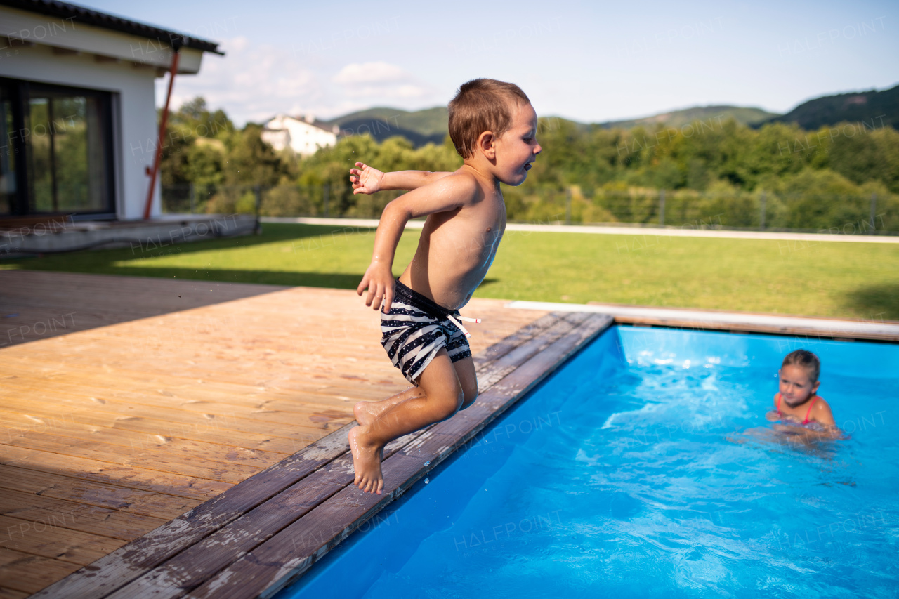 Two small children playing and jumping in swimming pool outdoors.