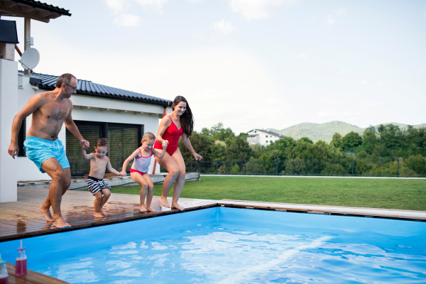 Young family with two small children by swimming pool outdoors, holding hands. Copy space.