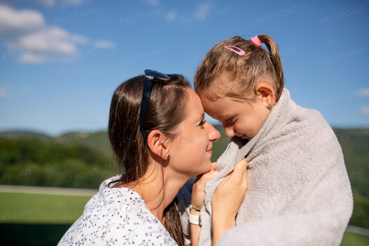 Side view of mother drying daughter with towwl outdoors after swimming.