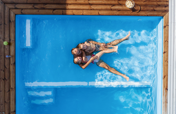 Top view of father with two small children sitting in swimming pool outdoors.