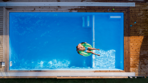 Aerial view of man with sunglasses lying in water in swimming pool outdoors.