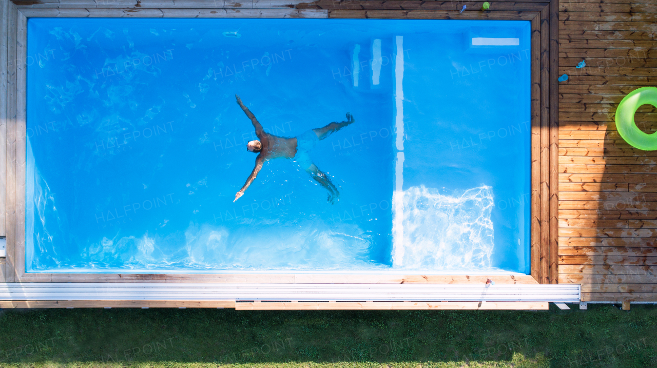 A top view of man swimming in water in swimming pool outdoors.