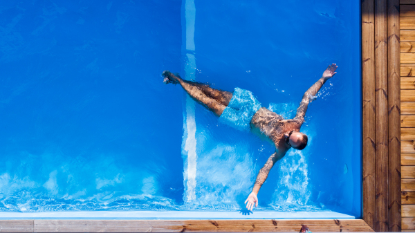 Top view of man with sunglasses lying in water in swimming pool outdoors.