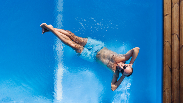 Top view of man with sunglasses lying in water in swimming pool outdoors.