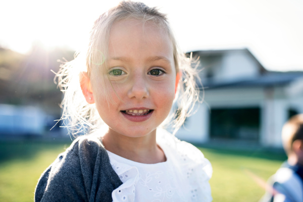 A front view of small girl standing outdoors, looking at camera.