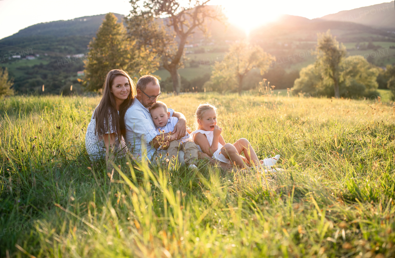 Happy young family with two small children sitting on meadow outdoors at sunset.