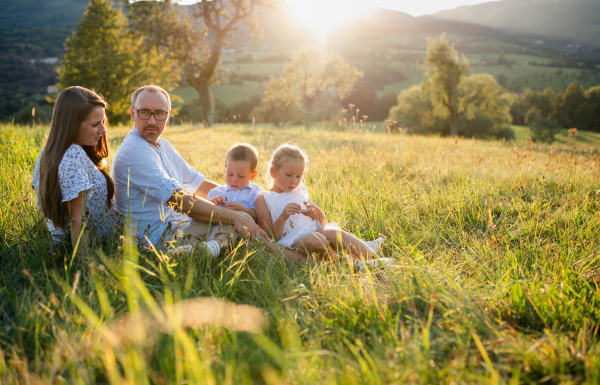 Happy young family with two small children sitting on meadow outdoors at sunset.