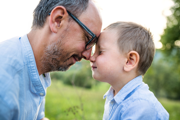 Side view of father with small toddler son on meadow outdoors, hugging.