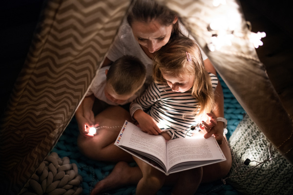 Top view of mother with children sitting indoors in bedroom, reading a book.