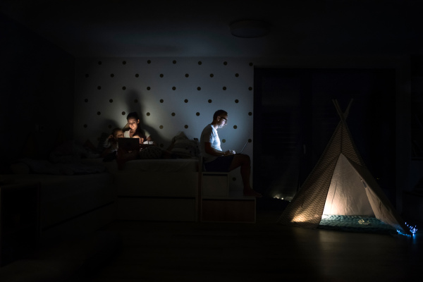 Young family with children sitting indoors in bedroom, using laptop.