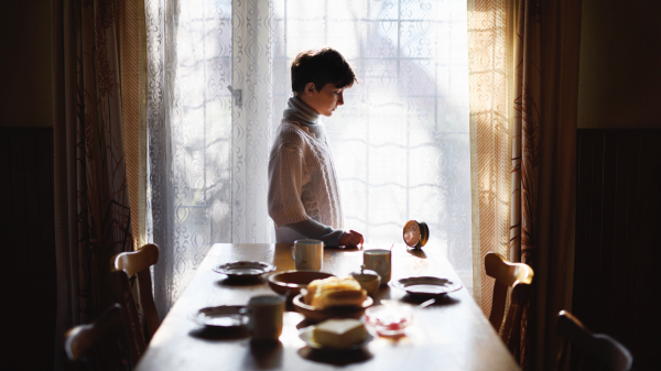 Portrait of poor sad small girl setting table indoors at home, poverty concept.