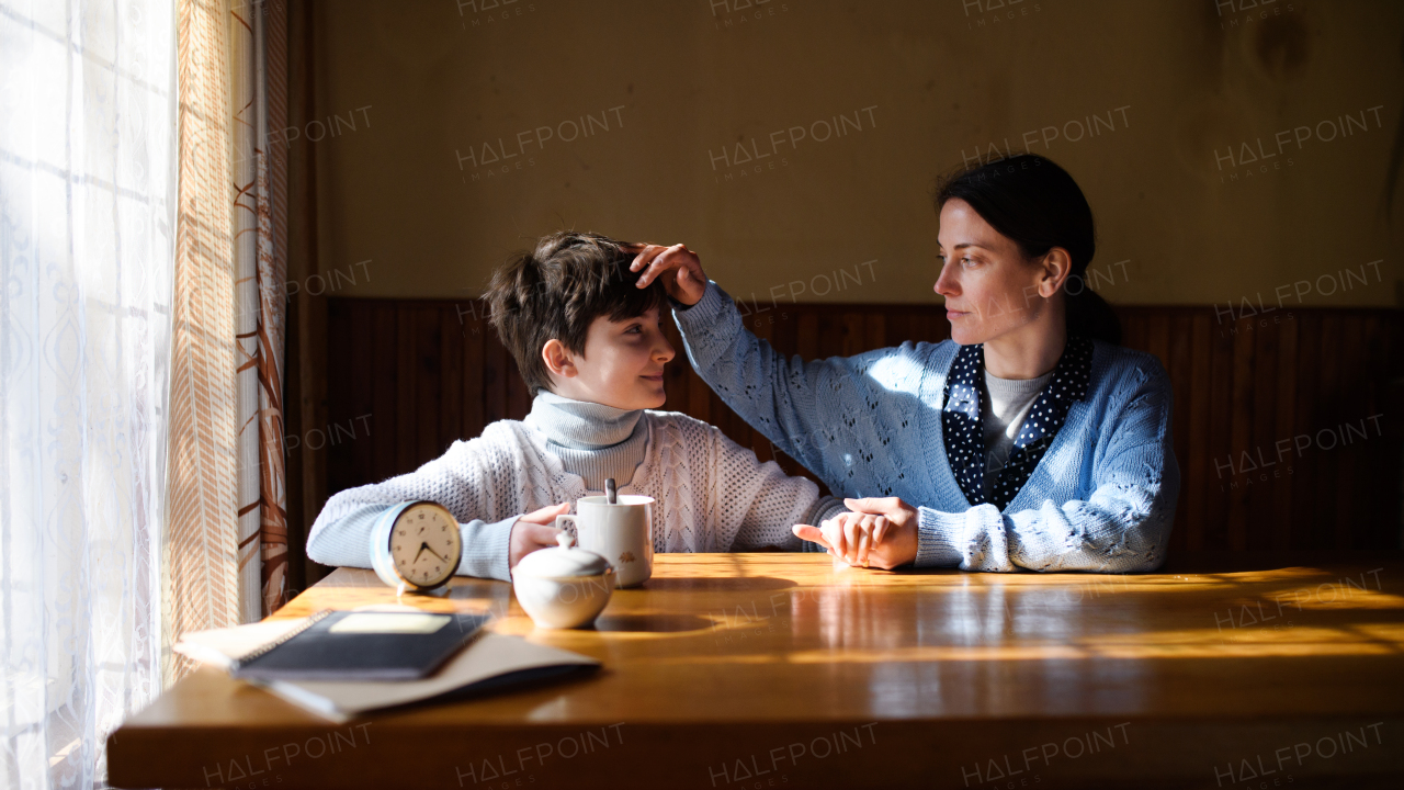 A portrait of sad poor mature mother talking to small daughter indoors at home, poverty concept.