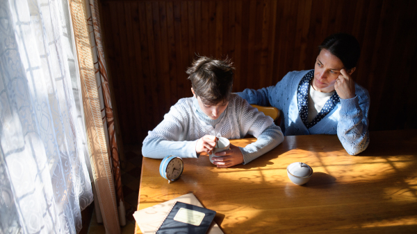 A portrait of sad poor mature mother talking to small daughter indoors at home, poverty concept.