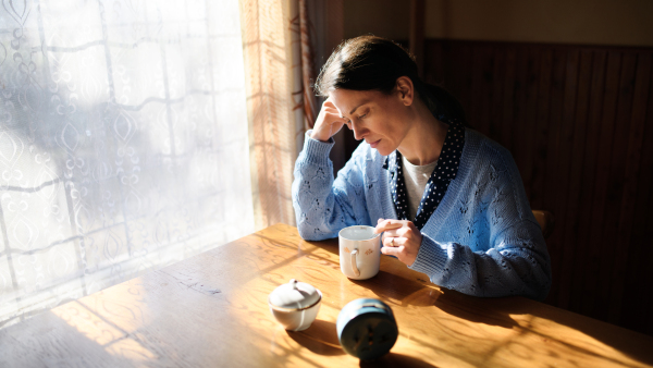 Portrait of unhappy poor mature woman with coffee indoors at home, poverty concept.