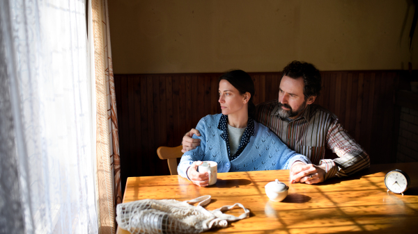 Portrait of poor mature couple sitting indoors at home, poverty concept.