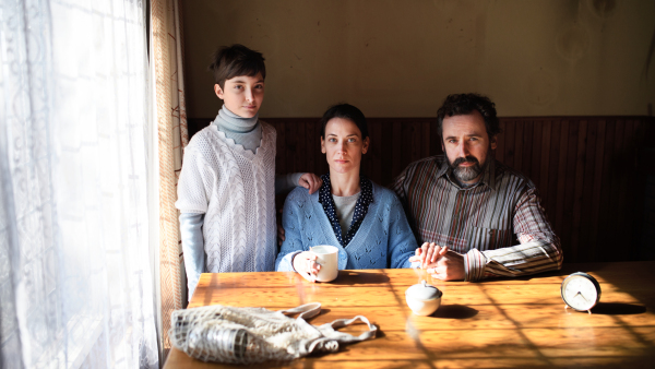 Portrait of poor mature couple with small daughter indoors at table at home, poverty concept.