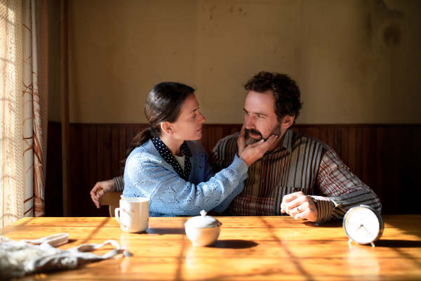 Portrait of poor mature couple in love sitting indoors at home, poverty concept.