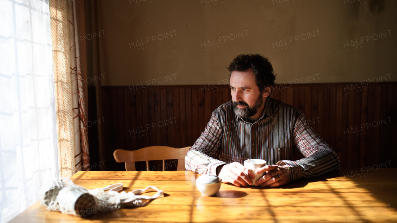 Portrait of unhappy poor mature man with coffee reading newspapers indoors at home, poverty concept.