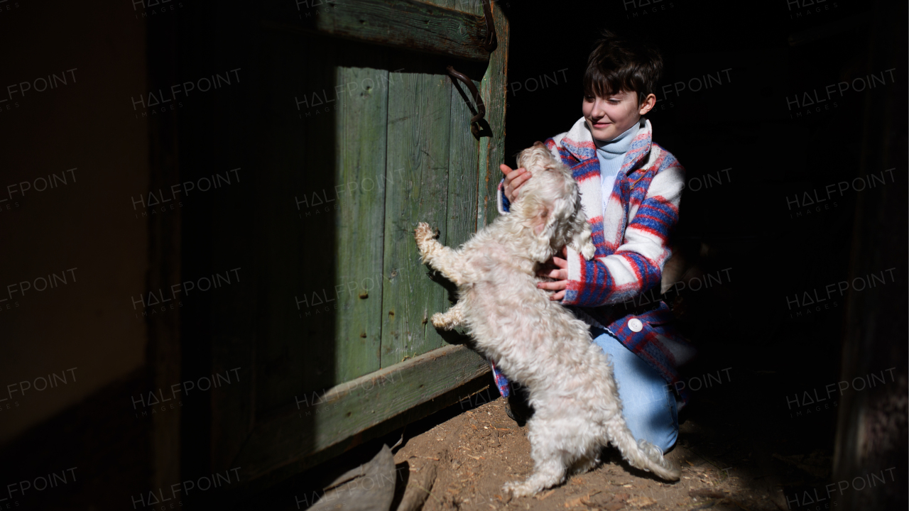 Poor happy small girl playing with dog outdoors in front of house, poverty concept.