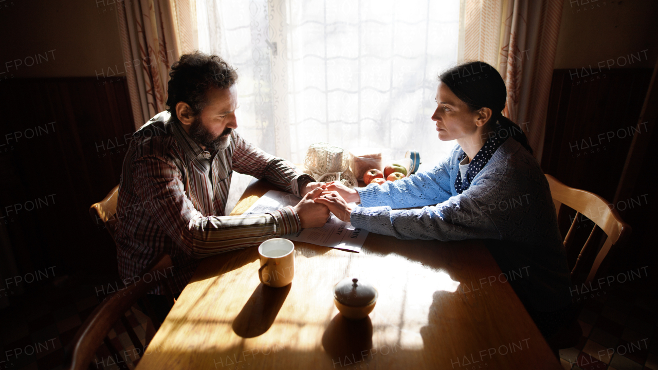 Portrait of sad poor mature couple holding hands indoors at home, poverty concept.