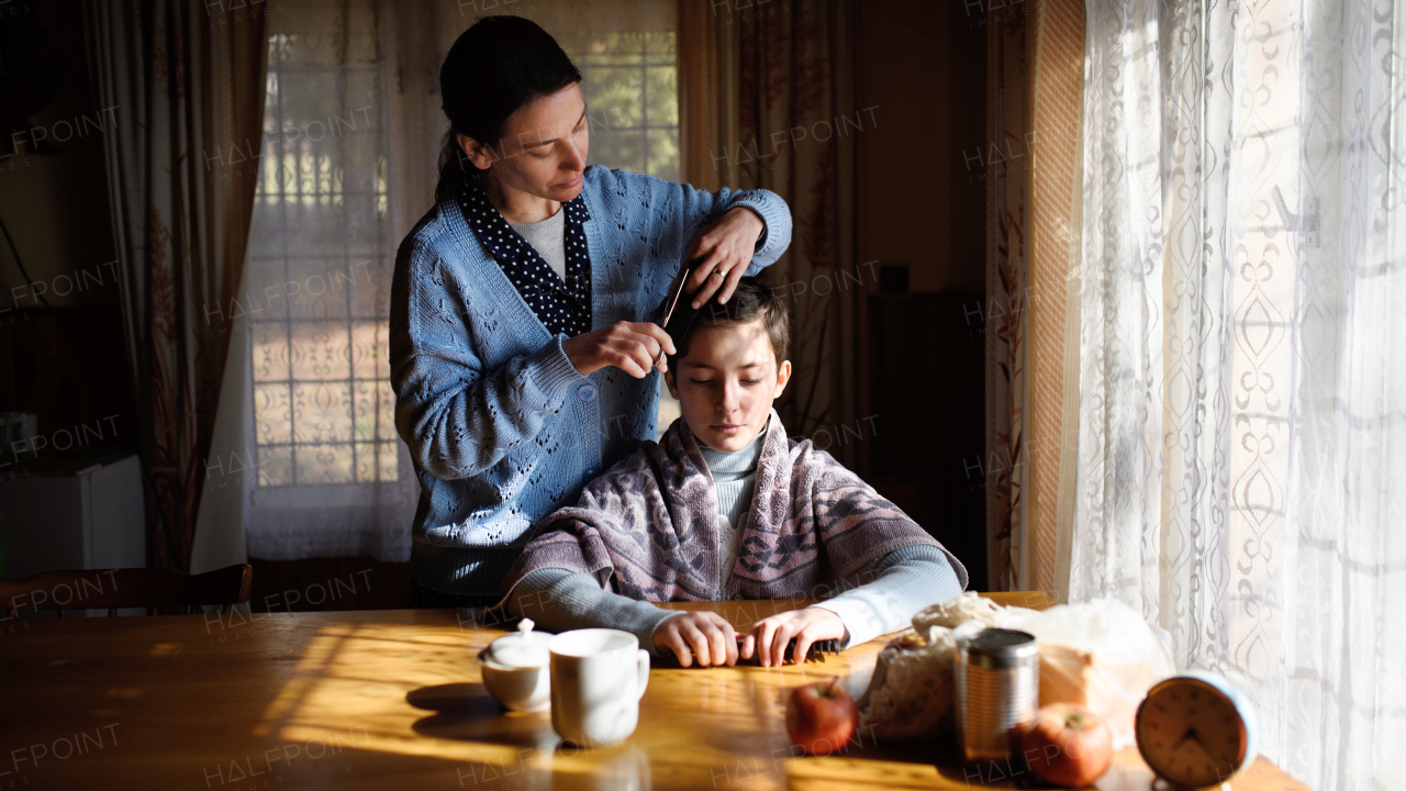 Portrait of sad poor woman cutting daughter's hair indoors at home, poverty concept.