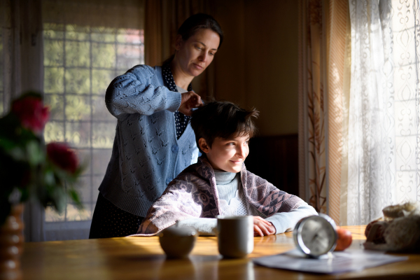 Portrait of sad poor woman cutting daughter's hair indoors at home, poverty concept.