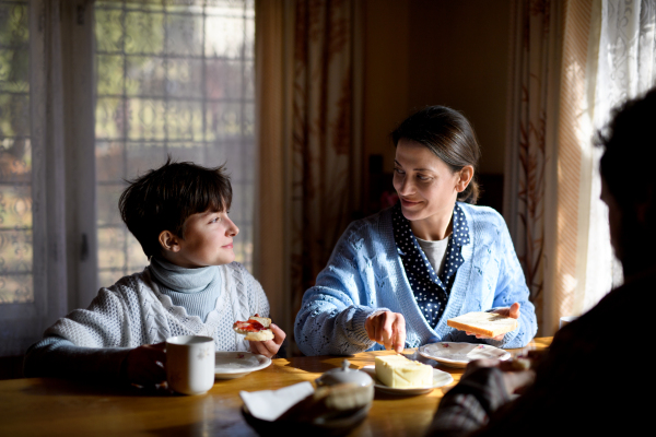 A portrait of happy poor sad small girl with parents eating indoors at home, poverty concept.