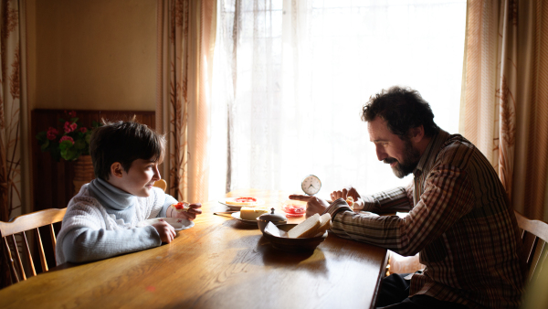 A portrait of poor small girl with father eating indoors at home, poverty concept.