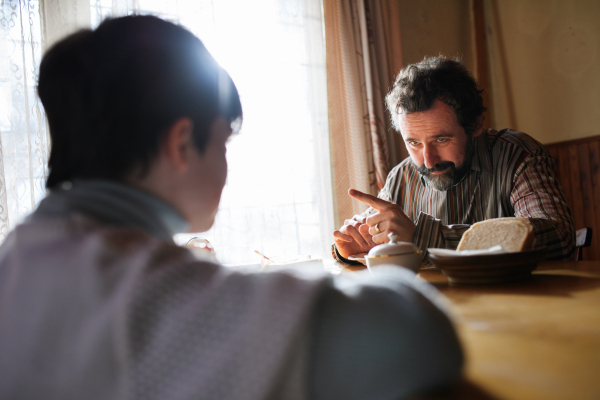 Rear view of a poor small girl with father eating indoors at home, poverty concept.