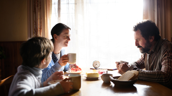 A portrait of poor sad small girl with parents eating indoors at home, poverty concept.