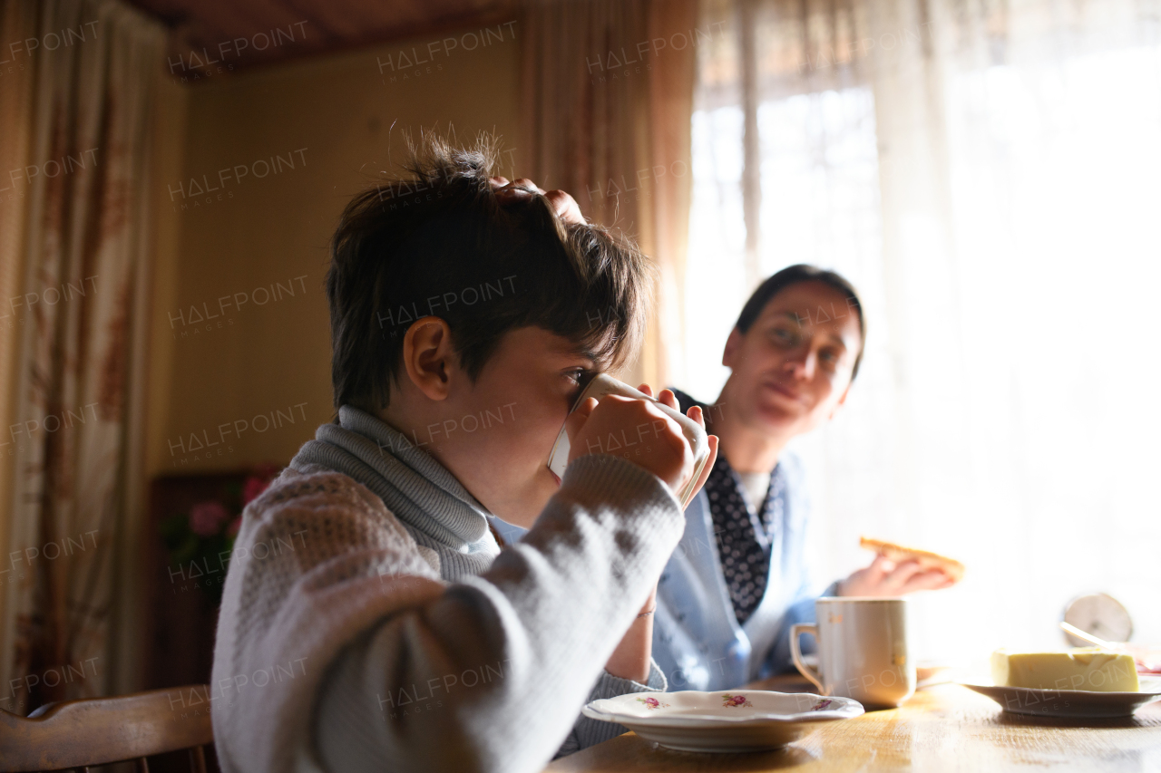 A portrait of poor small girl with mother eating indoors at home, poverty concept.