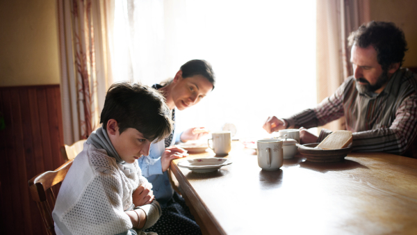 An angry small girl with parents sulking indoors at the table at home, poverty concept.