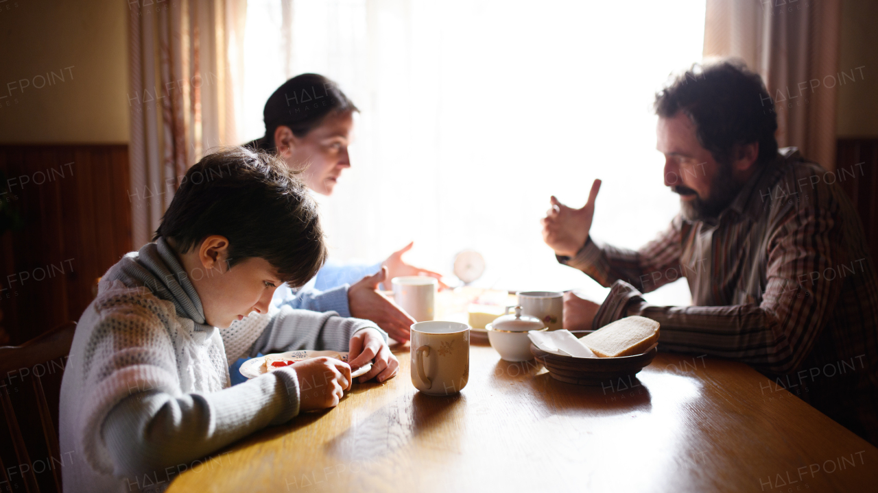 Portrait of poor sad small girl with parents eating indoors at home, poverty concept.