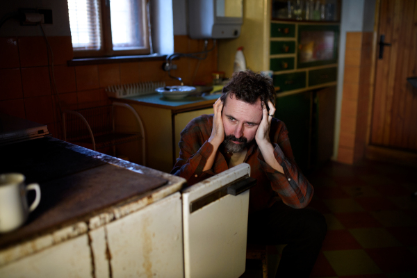 A portrait of sad poor mature man sitting indoors at home, poverty concept.