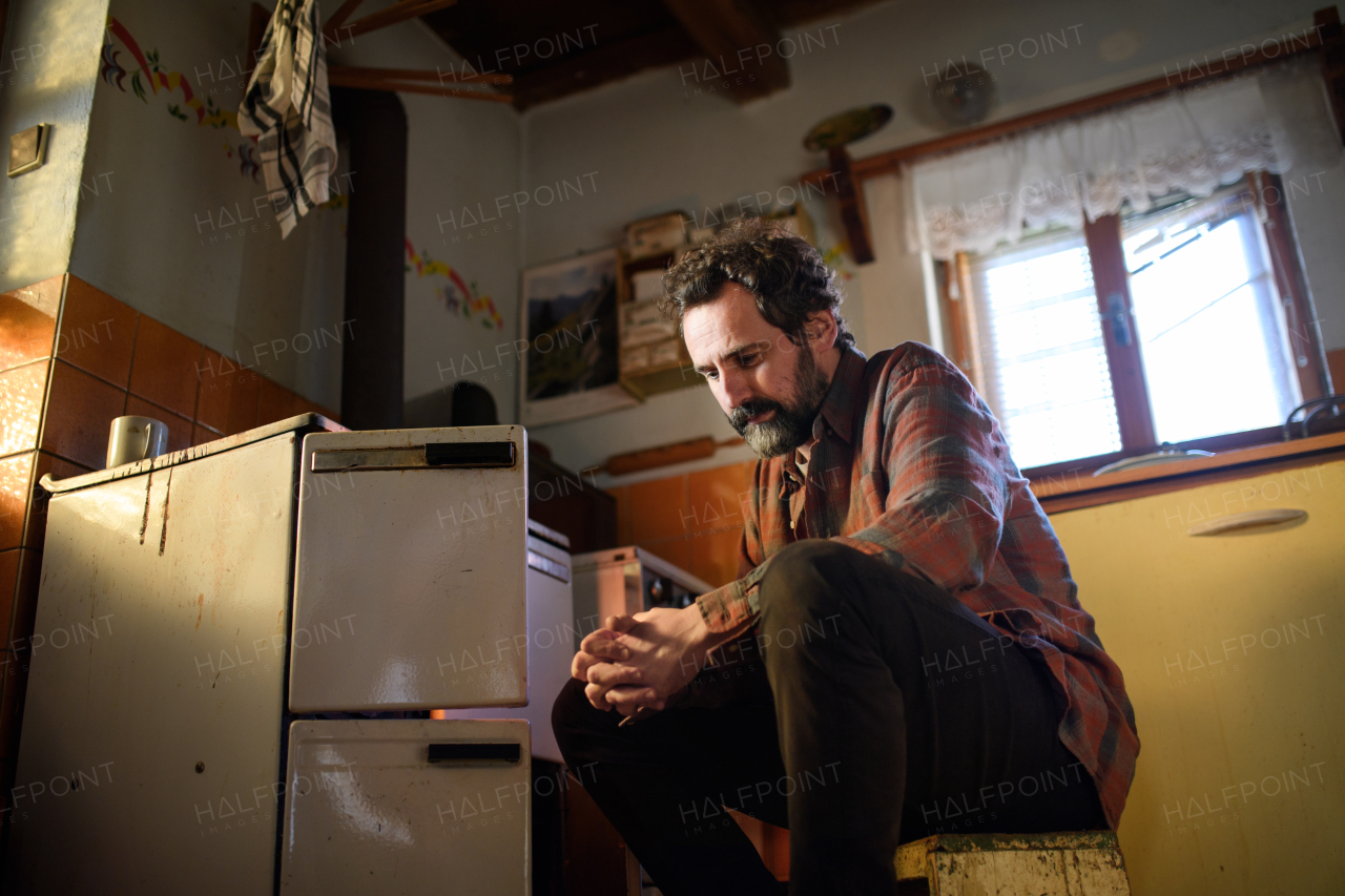 A portrait of poor mature man sitting indoors at home, poverty concept.